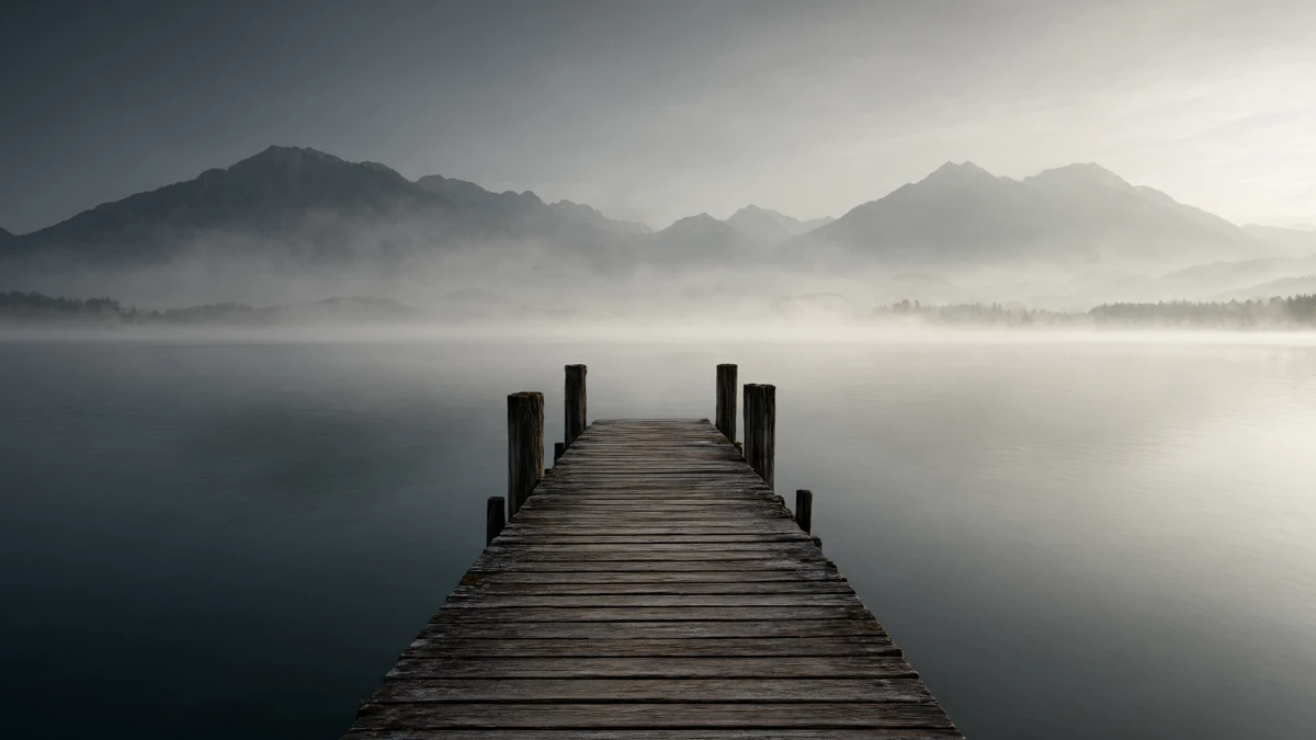 Holzsteg am Chiemsee im Morgennebel mit Blick auf das ruhige Wasser und die Chiemgauer Alpen, Sinnbild für Meditation am Chiemsee-Steg.